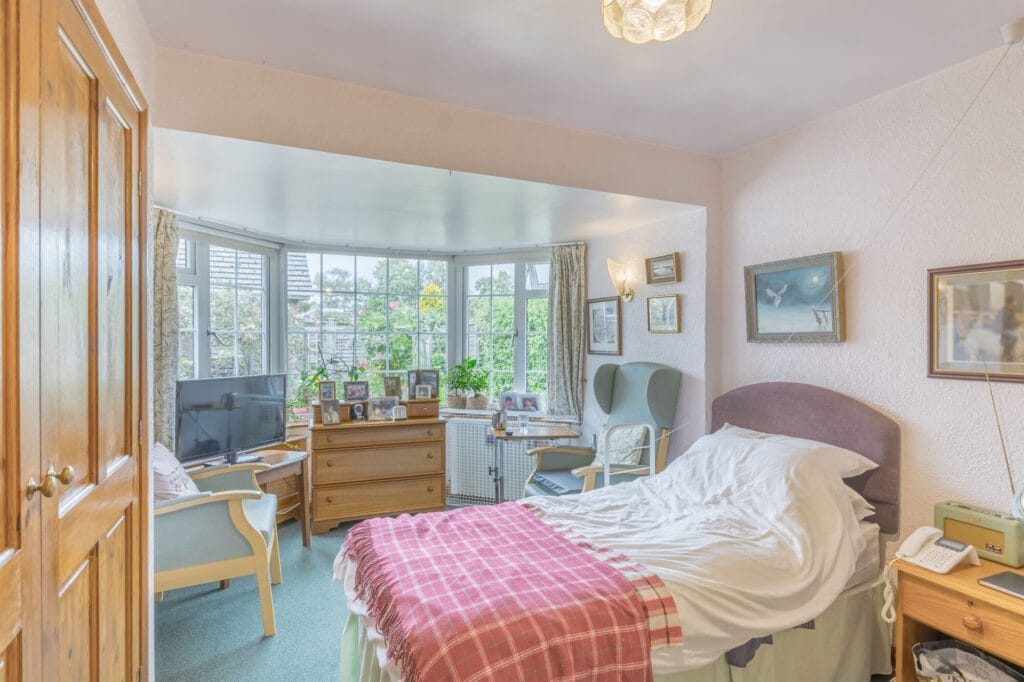 A resident’s bedroom at Arden House with a bay window and personal pictures on the walls